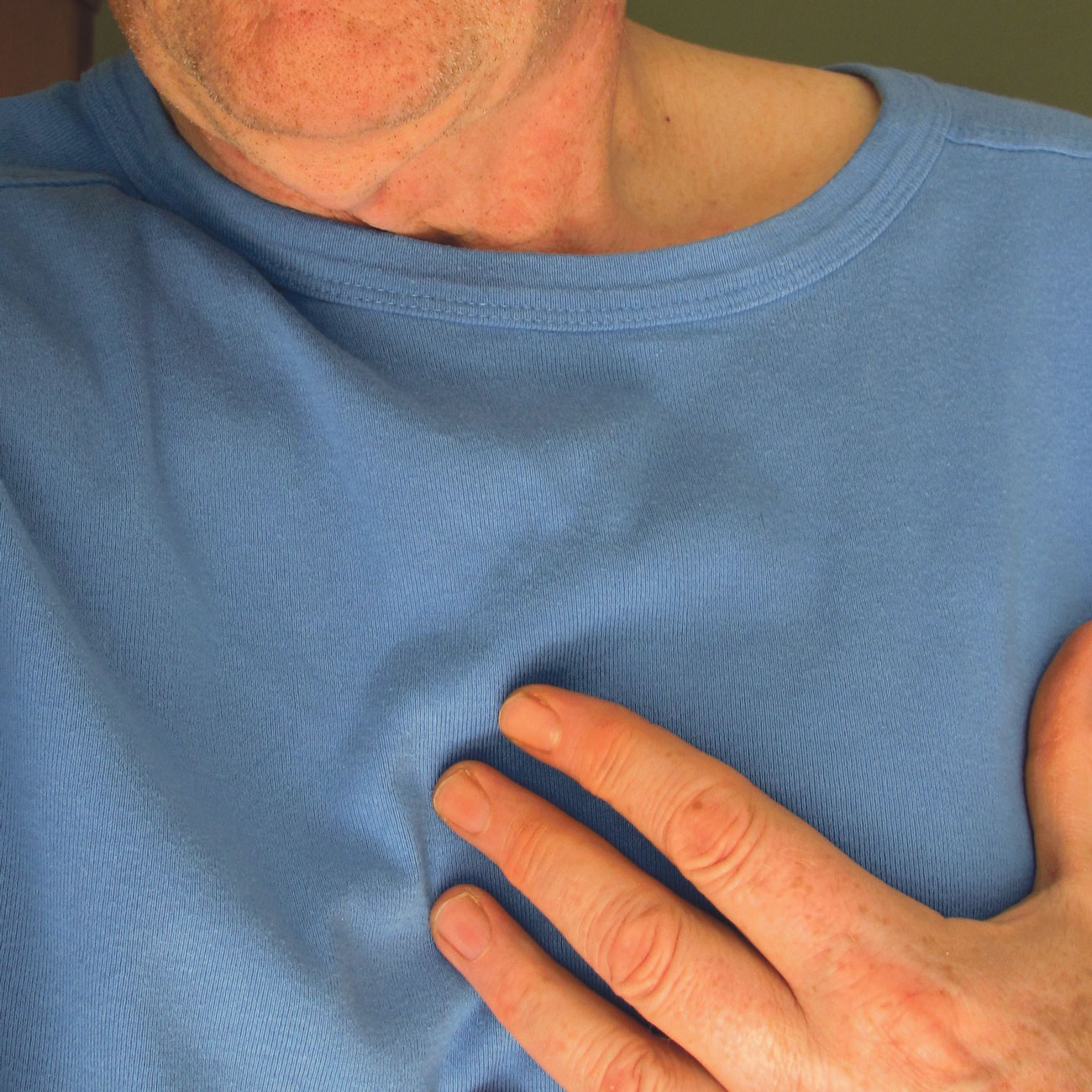 Nahaufnahme: Brustbereich eines Patienten, der die Hand auf das Herz gelegt hat.